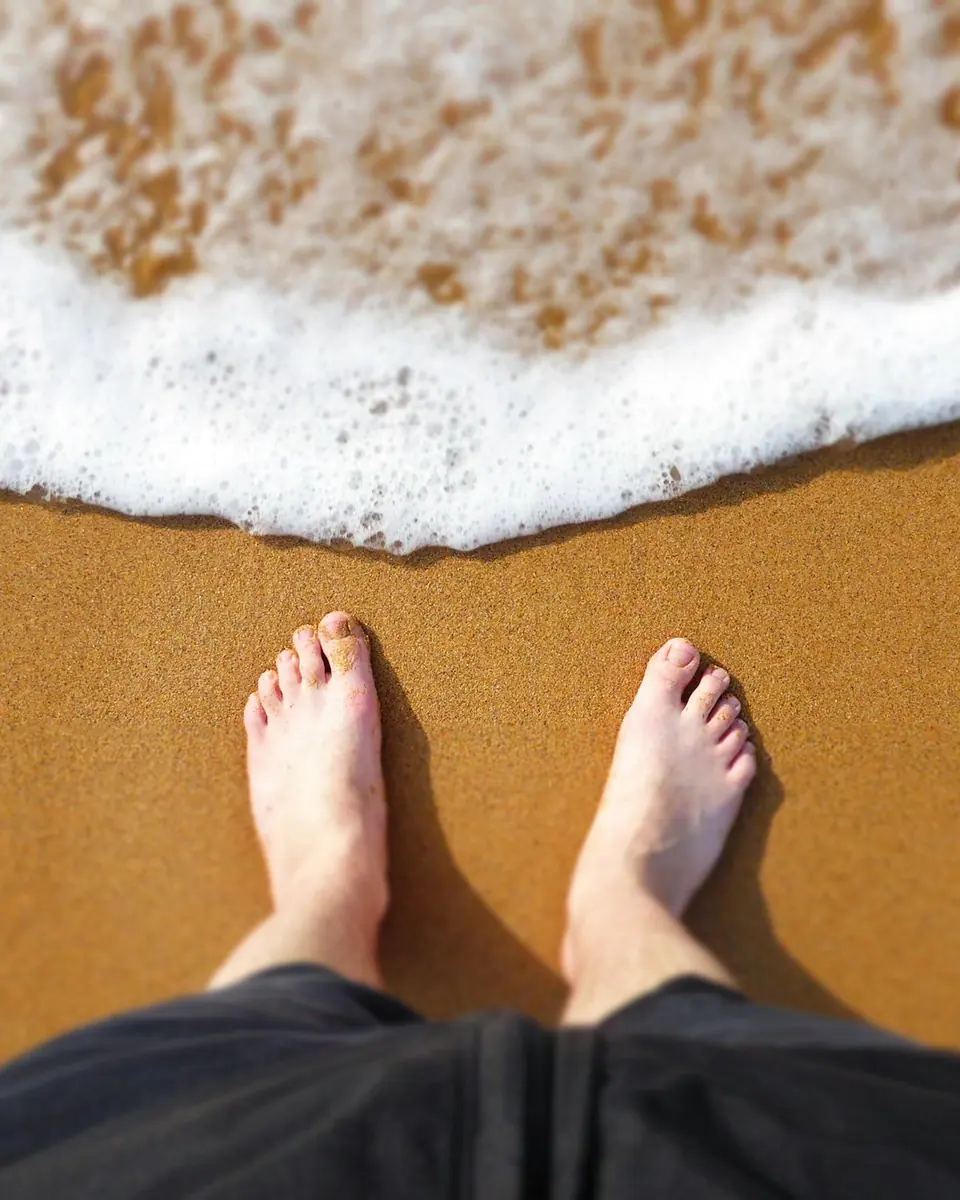 Des pieds nus sur le sable doré, face à l'écume d'une vague qui arrive